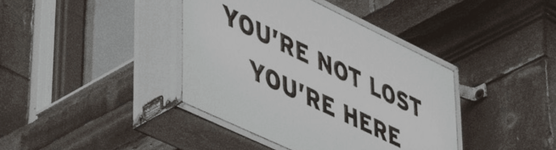 Sign with the text "You're Not Lost, You're Here" on a building wall