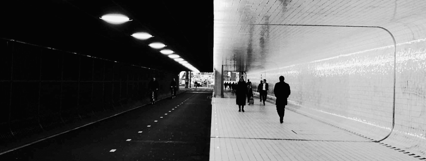 Split image of people walking through a contrasting tunnel with one dark and one brightly lit side