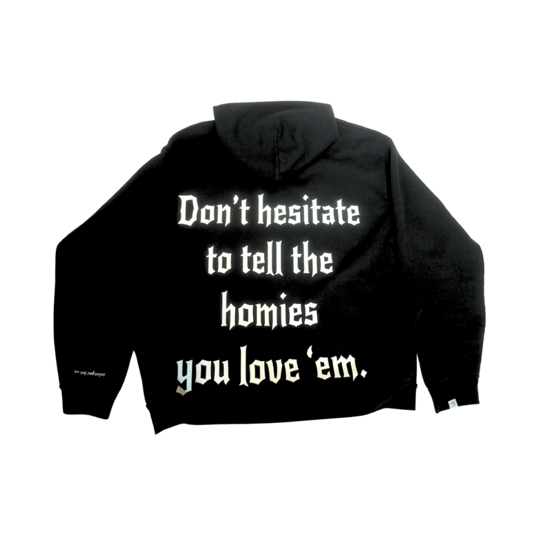 Black hoodie with bold message "Don't hesitate to tell the homies you love 'em" promoting love and appreciation among friends.